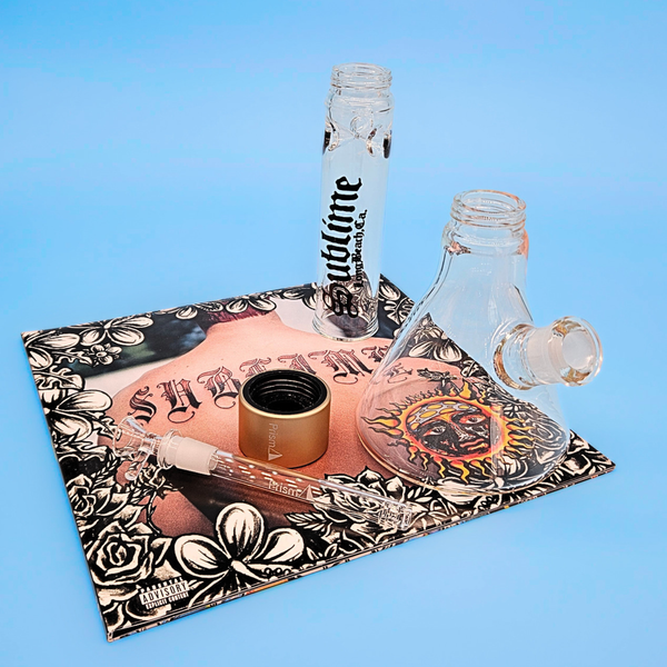 A high-quality lifestyle photo of the Prism Water Pipes and Sublime band collab. The white glass beaker with gold connectors is positioned in front of a stage-ready kick drum, merging the worlds of high-end smoking accessories and iconic 90s ska-punk culture. Ideal for collectors looking for genuine Sublime band gear.