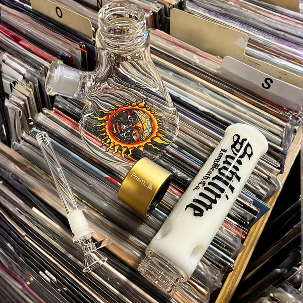 The Prism x Sublime official clear modular beaker bong sitting backstage at the legendary Red Rocks Amphitheatre. The 14mm downstem is removed to demonstrate the modular functionality of the piece, allowing fans to see the gold Halo Connector and the clear glass construction against the backdrop of the famous Colorado music venue.