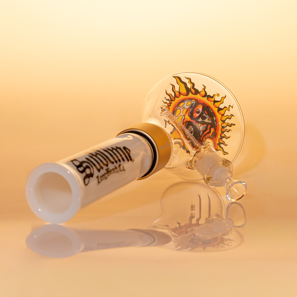 Official Sublime band merchandise: White modular tall beaker bong by Prism Water Pipes, pictured backstage on a guitar amp. This lifestyle shot confirms the official licensing, featuring the iconic Opie Ortiz sun logo and "Sublime Long Beach" branding. Ideal for collectors searching for "authentic Sublime glass" and "official band collaboration smoking accessories" used on tour.